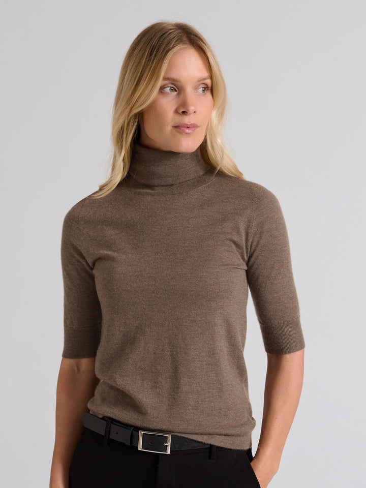 Woman wearing a brown turtleneck sweater against a gray background. Turtleneck cashmere t-shirt "Agnes" in 100% pure cashmere. Scandinavian design by Kashina. Color: Dark Toast.