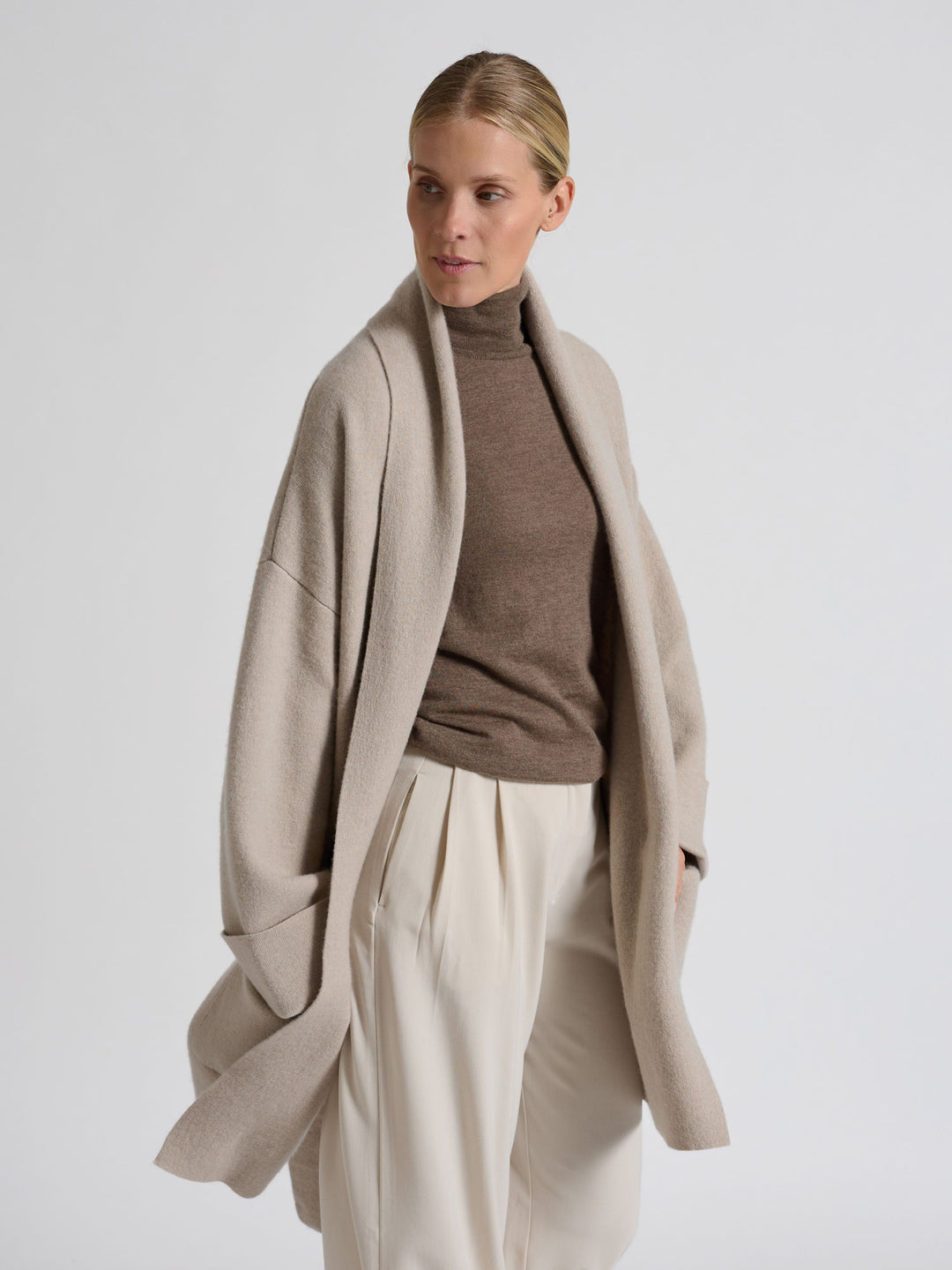 Woman wearing a brown turtleneck sweater against a gray background. Turtleneck cashmere t-shirt "Agnes" in 100% pure cashmere. Scandinavian design by Kashina. Color: Dark Toast.