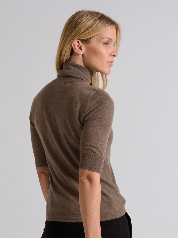 Woman wearing a brown turtleneck sweater against a gray background. Turtleneck cashmere t-shirt "Agnes" in 100% pure cashmere. Scandinavian design by Kashina. Color: Dark Toast.