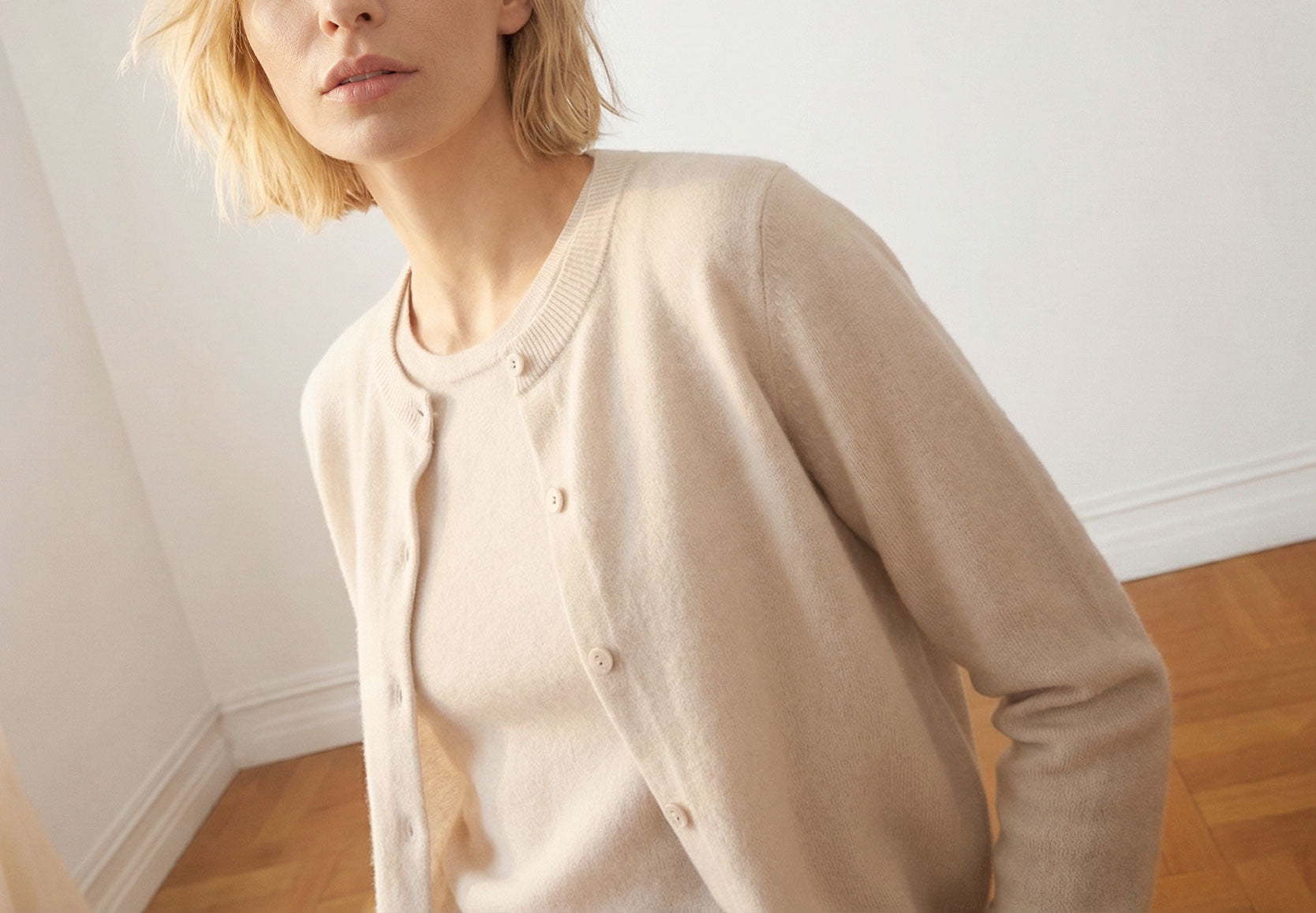 Woman wearing a creme cashmere cardigan in a minimal indoor setting